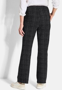 Pantaloni neri a fantasia con un design testurizzato, caratterizzati da strisce bianche verticali. Vita elastica e taglio dritto, indossati con sneakers chiare.