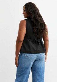 Top sin mangas de lino negro con un bodice ajustado, detalle de lazo en la espalda y dobladillo relajado, combinado con unos vaqueros de denim azul claro de cintura alta.