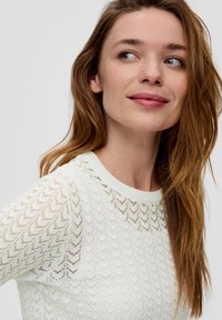 Sweter dzianinowy w jasnym miętowym kolorze, z teksturowanym wzorem falistym, krótkimi rękawami i okrągłym dekoltem, z detalami z otworami w dzianinie.