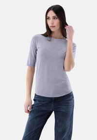 Helles graues, kurzärmliges Oberteil mit Rundhalsausschnitt, aus einem weichen Material gefertigt. Kombiniert mit dunkelblauen, leicht lockeren Jeans.