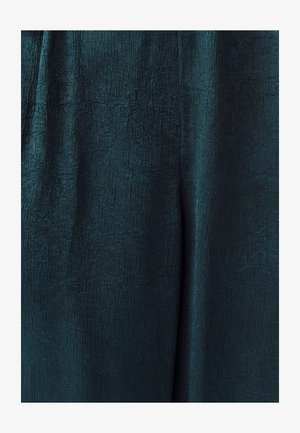 Türkisfarbener Stoff mit einer strukturierten, gekräuselten Oberfläche, der subtile Schimmer- und Musterabweichungen aufweist und sich für Kleidung oder Polsterungen eignet.