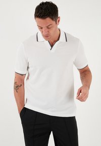 Hvid polo shirt med tekstureret stof, korte ærmer, en to-knaps placket og marineblå detaljer på kraven og ærmeenderne.