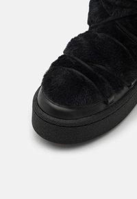 Zwarte sneaker met een zachte bovenkant met een gestructureerde afwerking, een ronde neus en een dikke rubberen zool met een patroon.
