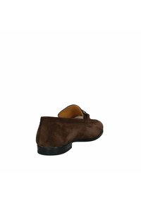 Scarpa in suede marrone senza lacci, con profilo basso, punta arrotondata e un piccolo dettaglio decorativo a fibbia vicino alla parte superiore. Suola in gomma nera.