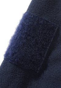 Tissu bleu marine foncé avec une pièce carrée en Velcro partiellement décollée, montrant la surface texturée du système de fixation à crochets et boucles.