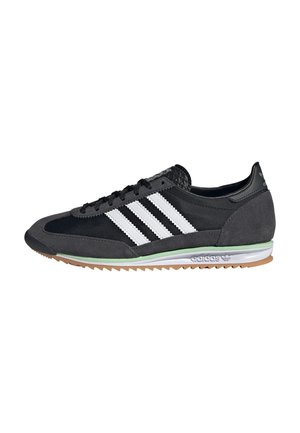 Czarno-szare buty sportowe Adidas z białymi paskami, czarnymi sznurowadłami, zielonym akcentem na śródpodeszwie oraz beżową, karbowaną gumową podeszwą zewnętrzną.