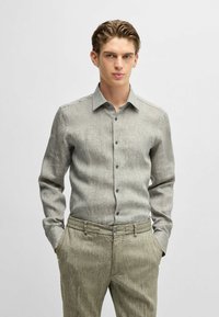 Camicetta grigio chiaro a maniche lunghe con tessuto texturizzato, colletto abbottonato e bottoni frontali, abbinata a pantaloni a righe verde chiaro.
