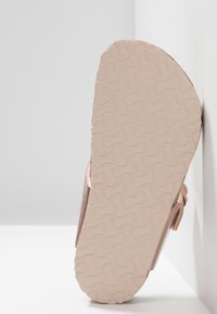 Sandal in oro rosa con una suola in gomma rosa chiaro texturizzata, caratterizzata da un motivo ondulato, e una parte superiore liscia.