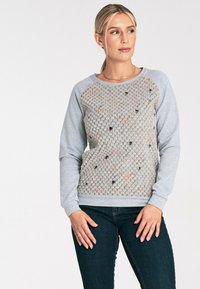 Szary sweter z teksturowanym, wzorzystym przodem i gładkimi rękawami. Posiada okrągły dekolt i ściągacze, zestawiony z ciemnymi dżinsami.