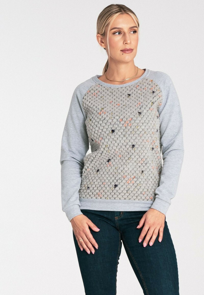 Szary sweter z teksturowanym, wzorzystym przodem i gładkimi rękawami. Posiada okrągły dekolt i ściągacze, zestawiony z ciemnymi dżinsami.