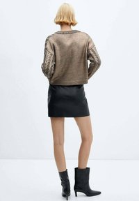 Bronzen gebreide trui met gevlochten mouwen, cropped ontwerp. Gecombineerd met een zwarte leren minirok en zwarte enkellaarsjes.