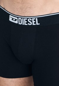 Boxers noirs avec une large ceinture contrastante en blanc portant le logo "DIESEL". Fabriqués en tissu extensible, avec un design de poche ajustée.