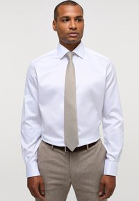 Wit overhemd met een puntig kraag, lange mouwen en knopenmanchetten, gecombineerd met een gestructureerde lichtbruine stropdas en beige broek.