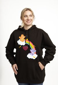 Černá mikina s kapucí s barevným grafickým designem zahrnujícím duhu, dva kreslené medvědy na mracích a srdíčkový přívěsek. Měkká tkanina s kapsou.