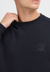 Mørkeblå crewneck sweatshirt med teksturfinish, med en subtil grafisk logo i grått på venstre brystområde.