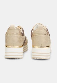 Pari sneaker platform beige dengan aksen emas dan sol putih serta beige bergaris, dilihat dari belakang di atas latar belakang putih.