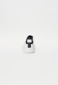 Adidași albi cu un exterior din piele netedă, accente negre pe calcă și pe patch-ul cu logo, talpă texturată și un design minimalistic.