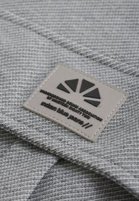 Grått tyg med rutmönster har en beige etikett präglad med en logo och texten "Indian Blue Jeans."