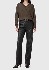 Oliwkowy sweter z dekoltem w serek i długimi rękawami, zestawiony z wysokim stanem czarnych skórzanych spodni oraz czarnych szpilek z zaostrzonym noskiem, ozdobionych paskiem z złotą klamrą.