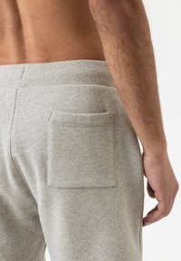Pantalons de survêtement en coton gris dotés d'une poche arrière unique, d'une taille élastique et d'une texture douce, vus de côté et de dos.