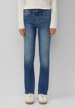 Jean en denim bleu avec une coupe droite, décoloration légère, style à cinq poches et fermeture à bouton, associés à des sneakers blanches.