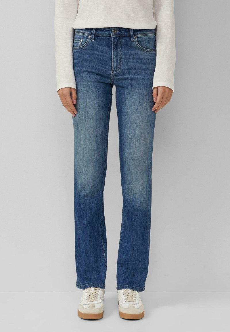 Blaue Jeans aus Denim mit geradem Beinschnitt, sanften Ausbleichungen, im Fünf-Taschen-Stil und mit einem Knopfverschluss, kombiniert mit weißen Sneakers.