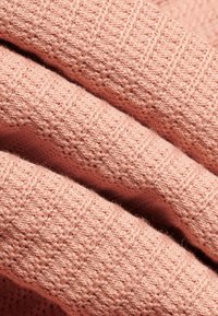 Detailný záber na jemnú ružovú pleteninu s textúrovaným vertikálnym pruhovým vzorom a malými tkanými diamantovými tvarmi.