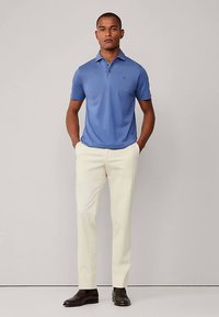 Modré polokošeľa svetlej farby s krátkymi rukávmi a klasickým golierom; v kombinácii s krémovými nohavicami a tmavohnedými topánkami. Jednoduchý dizajn bez vzorov.