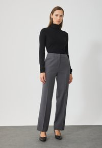 Pulover negru din lână cu guler înalt, purtat cu pantaloni gri cu croială. Pantalonii au picior drept și talie cu bucle pentru curea. Pantofi cu toc înalt negri.