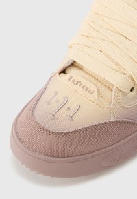 Αθλητικό παπούτσι με υφή από μπεζ και ανοιχτό ροζ υλικό, επενδυμένη γλώσσα, χοντρές κ ορδόνια και διακριτική λεπτομέρεια λογότυπου στο πλάι.