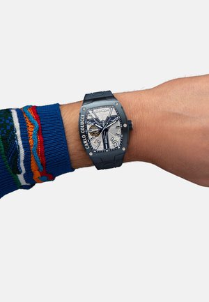 Black rubber strap watch with a rectangular silver and black dial, featuring bold numbers, ornamental details, and visible gears.