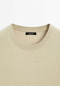 Pull beige à col rond avec un col côtelé montrant l’étiquette de la marque Massimo Dutti à l’intérieur de l’encolure.