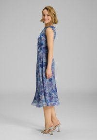 Blau und lila gemustertes Kleid mit tailliertem Oberteil und ausgestellt Rock. Aus leichtem Stoff gefertigt, verfügt es über kurze Ärmel und einen durchsichtigen Überzug.