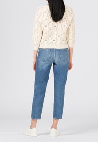 Pull en maille crème avec un motif texturé, manches trois-quarts, associé à un jean bleu clair taille haute et des baskets blanches.
