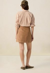 Jupe mini en velours côtelé marron associée à une chemise à rayures à boutons. L'ensemble comprend une casquette à imprimé léopard et des ballerines à motifs serpent.