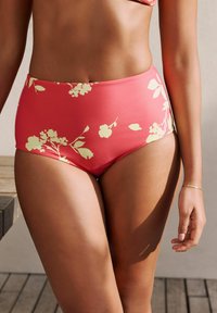 Visoko pasu bikini dno v koralni barvi z rumenim cvetličnim vzorcem. Gladka tekstura, eleganten kroj in minimalni detajli z dodatki.