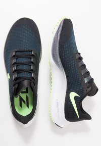 Nike urheilusandaalit, musta ja teal-kangas päällinen, vihreät yksityiskohdat, teksturoitu pohja, nauhakiinnitys, näkyvä logo sivussa, pehmustettu sisäpohja.