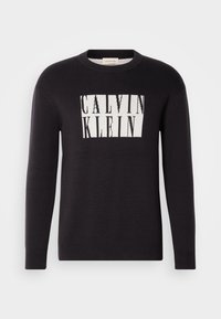 Black sweater featuring a crew neckline, long sleeves, and a white graphic print of the words "CALVIN KLEIN" across the front.