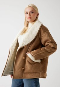 Giacca in eco-pelle scamosciata marrone con un ampio colletto in shearling bianco, due bottoni e tasche laterali, dal taglio rilassato e finitura testurizzata.