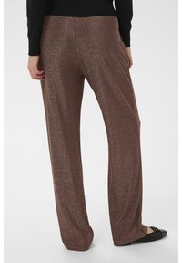 Barna fémes hatású, bőszárú nadrág csillogó textúrával; rugalmas derékpánttal és enyhén bővülő szárvéggel; fekete lapos cipővel párosítva.