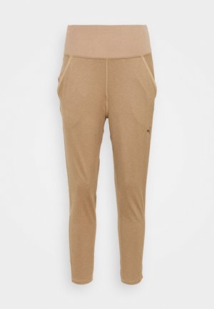 Pantalon de survêtement beige taille haute, coupe fuselée, avec poches avant et petit logo Puma noir sur la cuisse gauche.