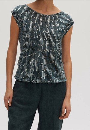 Ärmelloses Top mit grauem und weißem abstraktem vertikalem Rechteckmuster, getragen mit dunklen, hoch taillierten Hosen an einer stehenden Person.