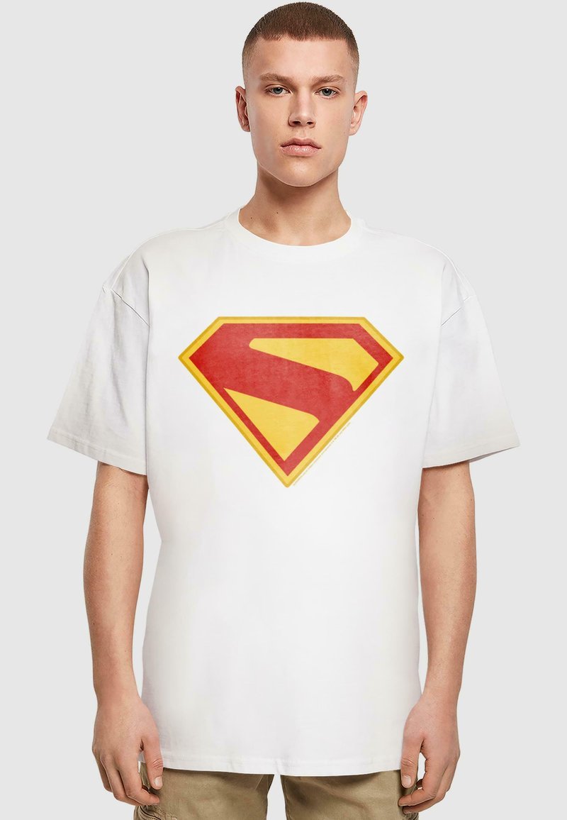 Fehér pamut póló, amelyen egy nagy piros és sárga Superman logó található az elején. A design klasszikus gyémánt alakot és élénk színeket tartalmaz.