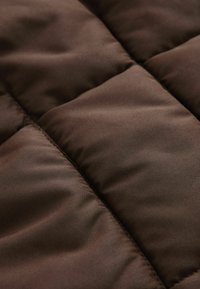 Tissu marron à texture matelassée, présentant des sections rembourrées douces et des coutures visibles, évoquant un design chaud et isolant.