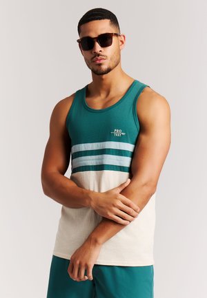 Türkisfarbenes und cremefarbenes Tanktop mit horizontalen Streifen in Hellblau und Dunkeltürkis. Weiches Baumwollmaterial. Modell trägt eine dunkle Sonnenbrille.