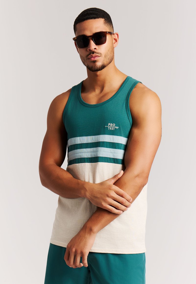 Camiseta sin mangas en tonos azul verdoso y crema con rayas horizontales en azul claro y azul verdoso oscuro. Material suave de algodón. Modelo con gafas de sol oscuras.