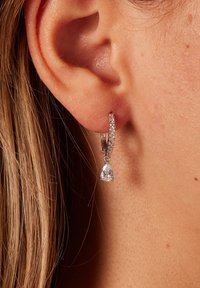 Zilveren oorring met een druppelvormige kristallen hanger, voorzien van een rij kleine heldere stenen langs de rand van de ring.