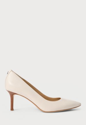 Une chaussure à talon haut pour femme de couleur crème, à bout pointu et talon aiguille en bois, sur un fond uni.