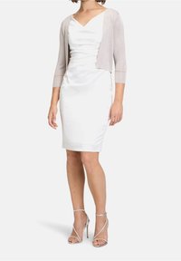 Vit satin klänning med en smickrande draperad halsringning och figurnära silhuett, i kombination med en ljusgrå, kort cardigan och silverfärgade remsandaler.