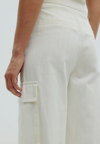 Witte wijde broek met een gemêleerde afwerking, voorzien van een zijvak en achterzakken. Netjes afgewerkte naden en een getailleerde pasvorm.